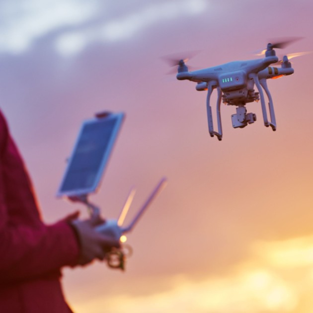 A person in a red jacket operates a drone with a remote control during sunset.